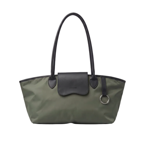 An olive green nylon tote bag with black leather handles, trim, and a front flap pocket, featuring a silver-tone metal O-ring, photographed on a light gray background.