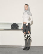 Woman wearing a white crop top, gray leggings, and black shoes holding a black and white patterned bag.