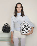 Person holding a white helmet and black bag against a plain background