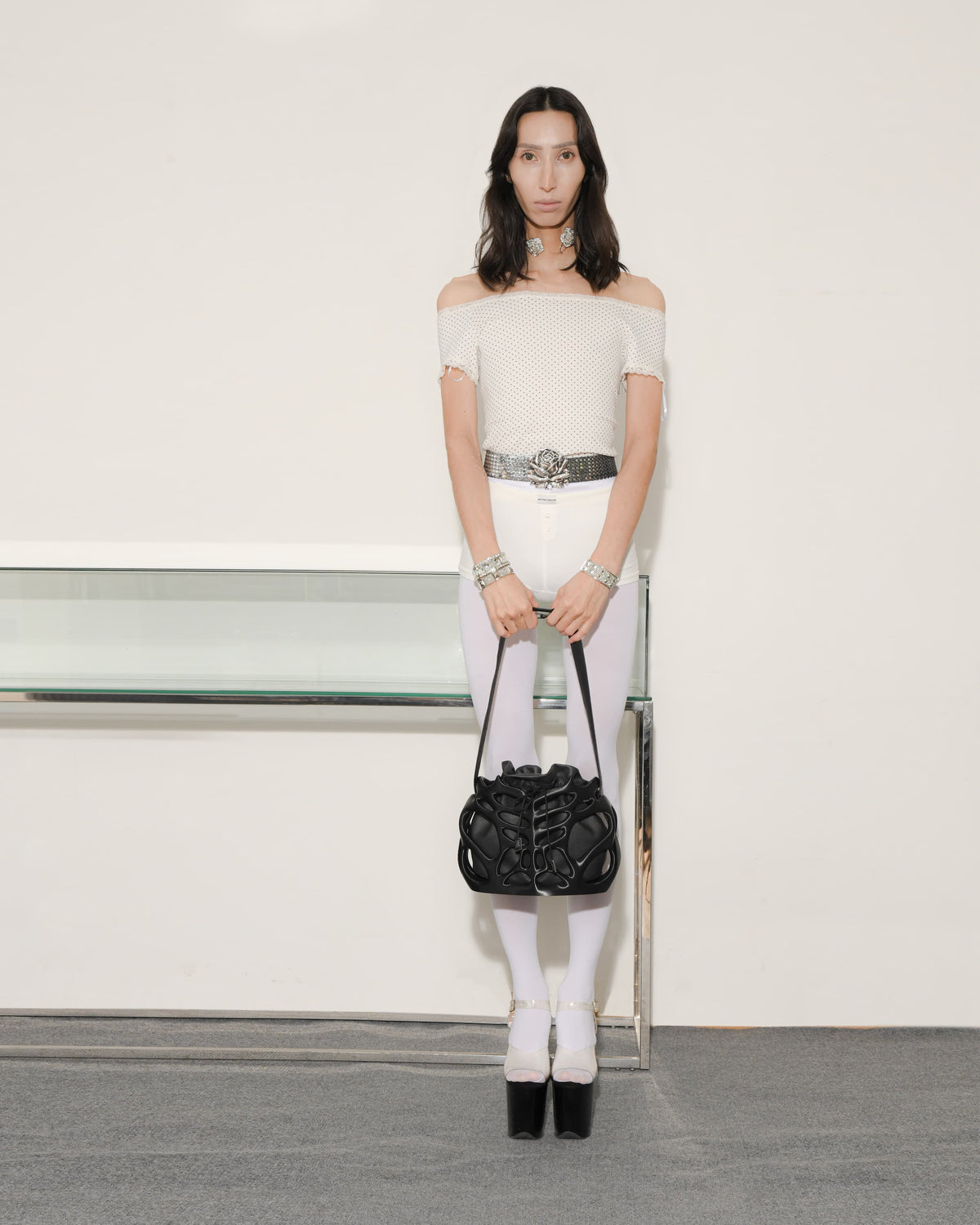 Woman in a white outfit with a black handbag against a plain background