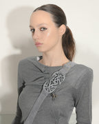 Woman wearing a gray sweater with a decorative brooch against a white background